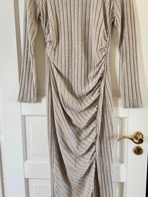 Beige ribbad långklänning från SHEIN - Trendig beige långklänning från SHEIN med ribbad struktur och snygg rynkning framtill. Klänningen har långa ärmar och en smickrande slits på sidan. Perfekt för dig som gillar en stilren och modern look.