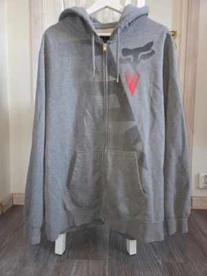 Fox Hoodie - Grå hoodie med fickor, dragkedja och luva från märket Fox. Storlek XL. Det finns tecken på använd, nopprig och lite skavanker på metallen på snöret men annars fint skick.   #foxracing #foxhoodie #menswear #herrkläder #streetwear #streetwearstyle #casualwear #urbanstyle #cleanlook #simpleoutfit #comfywear #everydayoutfit #hoodie #ziphoodie #hoodiestyle #layering #vinterplagg #basplagg #y2k #90s #00s #2000s #retrostyle #retroinspo #trendy #fashiontrend #styleinspo #mensoutfit #outfitmen