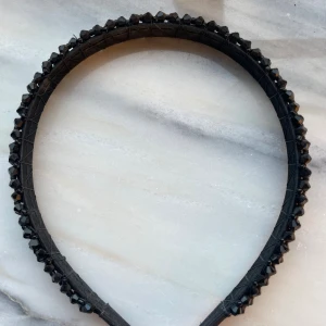 Svart diadem med nitar - Snyggt svart diadem med små svarta nitar längs hela bågen. Diademet har en klassisk form och funkar som en perfekt accessoar. 