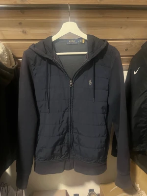Ralph lauren cardigan - Snygg marinblå hoodie från Polo Ralph Lauren med dragkedja framtill och broderad logga på bröstet. Huva med dragsko och quiltad frontpanel som ger en sportig look. Ärmar och rygg i mjukt sweatshirtmaterial. Perfekt för en avslappnad stil.