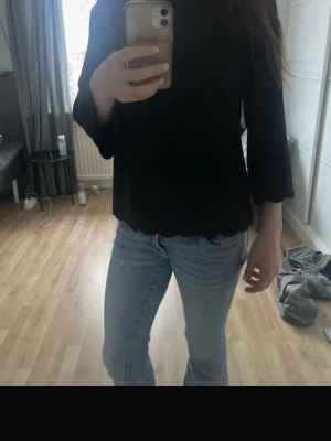 Svart topp med vågig kant - En svart långärmad topp med rund hals och vågiga kanter vid ärmslut och nederkant. Toppen har en enkel och stilren design som passar till mycket. Materialet känns mjukt och lätt, perfekt för både jeans och kjol. Den är i storlek L men ni ser hur den sitter på mig som oftast brukar ha S