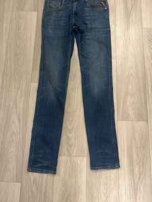 Blå jeans från Replay - Snygga blå jeans från Replay med klassisk femficksdesign och raka ben. Jeansen har en mörkblå tvätt med lätt slitna detaljer och kontrastsömmar. Perfekta för en avslappnad och trendig look. Storlek 30/34