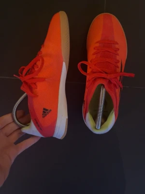 Adidas orange sneakers med vita sulor - Säljer ett par snygga sneakers från Adidas i en stark orange färg med svarta detaljer och vita sulor. Skorna har lågt skaft, snörning och ovandel i meshmaterial som andas. Perfekta för dig som gillar sportig stil och vill sticka ut.
