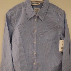 NY & OANVÄND klassisk blå - vit smalrandig Oxford blus/skjorta, dam. 34/XS-S. - Helt NY & OANVÄND fin klassisk blå-vit smalrandig Oxford-blus/skjorta från LOGG-avdelningen/H&M. Storlek: 34/XS-S. Material: Bomull. Helt felfri. Lappar/etiketter sitter kvar sedan inköpet. Nypris i butik är 199 kr. Modellen visar ungefär hur den ser ut på.