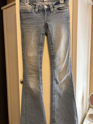 Ljusblå bootcut jeans från Gina - Snygga ljusblå bootcut jeans med klassisk femficksdesign och broderade detaljer på bakfickorna. Jeansen har en låg midja och är tillverkade i mjuk denim med lätt stretch för skön passform. Liten fläck som man kan se på bild 6 men den går nog bort om man tvättar dem. Storlek Xxs tall, jag är ca 172 som man kan se på bild 5 så är dem ganska långa om någon undrar över längden.