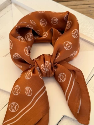 Cognac Monogram Scarf – quiet luxury & silkeslook - Elegant scarf i djup cognac caramel-ton med exklusivt monograminspirerat mönster och mjuk satinfinish. Den varma färgpaletten ger en sofistikerad och tidlös känsla med tydlig quiet luxury-estetik.  Lätt och följsam kvalitet med vacker silkeslook som faller elegant – perfekt runt halsen, i håret eller knuten på väskan för en chic couture-touch.  En stilren statement-accessoar i rich amber, creamy ivory och warm cinnamon-toner. 🤎  70x70