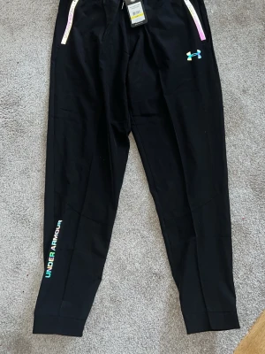 Under Armour Breathable Jogger Fit - *PRIS KAN DISKUTERAS PRIVAT* Säljer ett par helt nya Under Armour träningsbyxor med tags kvar. Den är reflective som man kan se i bilderna. Kan användas som mode, även till gym. Byxorna är i strlk L.  • Färg: Svart med diskreta logodetaljer • Passform: Regular fit • Material: Lätt och stretchigt funktionsmaterial • Resår i midjan + justerbar snörning • Dragkedjefickor • Perfekta för gym, löpning eller vardag  Aldrig använda. *PRIS KAN DISKUTERAS PRIVAT*