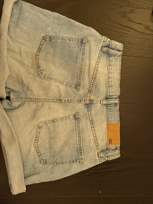 Ljusblå denimshorts från 157 - Snygga ljusblå denimshorts från 157 med klassisk femficksdesign, uppvikta benslut och hög midja. Perfekta för varma dagar och enkla att matcha med olika toppar. Jeansmaterialet ger en avslappnad och trendig look.