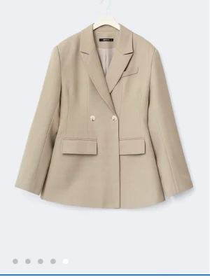 Shaped blazer från gina - Snygg beige kavaj från Zara med dubbelknäppning och klassisk krage. Kavajen har två stora fickor med lock framtill och en bröstficka. Materialet är slätt och strukturerat, perfekt för en stilren look.