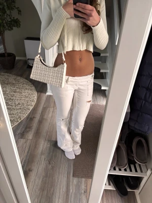 Vita low waist jeans med slitningar - Säljer ett par vita low waist jeans med raka ben och slitningar vid fickorna och knät. Jeansen har en klassisk femficksmodell och är tillverkade i denim med lite stretch för skön passform. Perfekta för dig som gillar en trendig och avslappnad stil.
