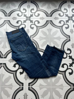 Mörkblå jeans från Replay - Säljer ett par snygga mörkblå jeans från Replay med klassisk femficksdesign och raka ben. Jeansen har subtila slitningar och detaljer i silverfärg vid fickorna. Perfekta för en avslappnad och trendig look. Klippta längst ner. MVH EA
