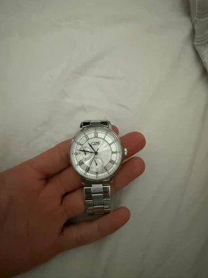 Silverfärgad klocka från GHW - Stilren klocka från GHW i silverfärg med klassisk länkarmband i metall. Urtavlan är rund med romerska siffror och flera små urtavlor för extra funktioner. Perfekt accessoar för dig som gillar en tidlös och elegant look.