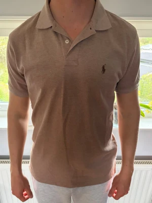 Beige pikétröja från Polo Ralph Lauren - Klassisk beige pikétröja från Polo Ralph Lauren med korta ärmar och krage. Tröjan har en broderad logga på bröstet och custom fit-passform. Perfekt till en avslappnad men ändå stilren look. Storlek L men sitter som en M👍🏼Nyskick!