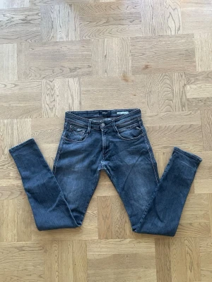 Replay anbass  - Snygga mörkgrå slim fit jeans från Replay med klassisk femficksmodell och diskreta slitningar. Jeansen har smal passform och detaljerade sömmar, perfekta för en trendig och avslappnad look. Mått på längden är 101cm, mått på bredden från midjan är 37cm