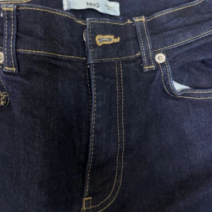 Mörkblå utsvängda jeans från MANGO - Snygga mörkblå jeans från MNG med utsvängda ben och klassiska kontrastsömmar. Jeansen har hög midja och femficksmodell, perfekta för en trendig och avslappnad look. Tillverkade i denim med en stilren finish.