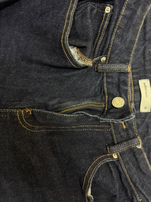 Mörkblå raka jeans från gina  - Snygga mörkblå jeans från gina med raka ben och klassiska kontrastsömmar. Jeansen har fem fickor, gylf med dragkedja och knapp samt bälteshällor. Perfekta för en stilren och avslappnad look.