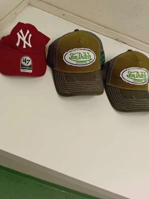Fyra kepsar från Von Dutch, NY & Oakley - Säljer fyra kepsar: två bruna Von Dutch med broderad logga, en röd New York Yankees från 47 Brand och en brun Oakley med svart logga. Alla kepsar har böjd skärm och justerbar passform. Perfekta accessoarer för en avslappnad streetstil.