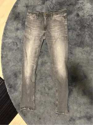 Grå replay slim fit jeans med slitningar - Snygga grå slim fit jeans med slitna detaljer och klassisk femficksdesign. Jeansen har dragkedjegylf och smal passform som sitter tajt längs benen. Perfekta för en avslappnad och trendig look.