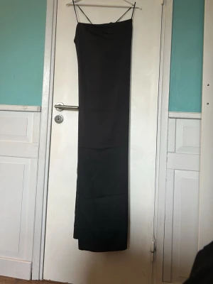 Svart lång klänning med tunna band - Stilren svart långklänning från åhlens med tunna axelband och knytning i ryggen. Klänningen har en smal passform och är tillverkad i ett glansigt, mjukt material som ger en elegant look. Perfekt för dig som gillar minimalistisk stil. Nypris 599