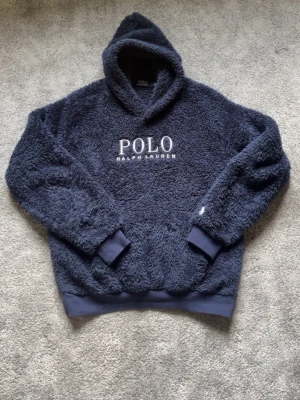 Ralph Lauren fleece hoodie - Fluffig och varm hoodie från Ralph Lauren. Inga defekter, sparsamt använd! Snören till hoodien saknas dock men är enligt mig dessutom snyggare så. Hör av er vid frågor!