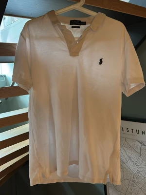 Vit pikétröja från Polo Ralph Lauren - Klassisk vit pikétröja från Polo Ralph Tröjan har den ikoniska broderade loggan på bröstet och knäppning vid halsen. Perfekt för en stilren och avslappnad look. Köpt här på plick men kom inte till användning. Inga defekter.