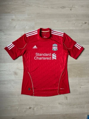 Liverpool FC Fotbollströja 2010/11 Hemmatröja Storlek M   - Mycket fin fotbollströja i röd färg. Tröjan är i mycket bra skick och sparsamt använda. |  Äkta som allt annat jag säljer! ✅ |  Storlek: M | Skick: Mycket Bra Skick - Tyvärr har trycket börjat släppt litegrann på sponsortexten (SE SISTA 2 BILDER) | Färg: Röd | Märke: adidas | Modell: Fotbollströja |   Hör gärna av dig vid frågor så svarar jag så fort jag kan! 😄
