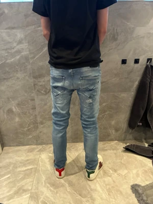 Ljusblå slitna skinny jeans replay  - Säljer ett par ljusblå skinny jeans med slitningar och hål på både fram- och baksida. Jeansen har klassisk femficksdesign och är tillverkade i stretchigt denimtyg för en tajt passform. Perfekta för en avslappnad och trendig look.