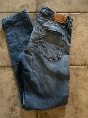 Blå jeans från Jack & Jones - Snygga blå slim fit jeans från Jack & Jones med klassisk femficksdesign och läderpatch bak i midjan. Jeansen har en lätt tvättad look och raka ben. Perfekta till en avslappnad stil och passar till det mesta i garderoben.