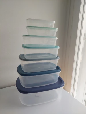 Set med plastburkar med lock - Säljer ett set med sex rektangulära plastburkar i olika storlekar. Burkarna är genomskinliga med lock i olika blå och turkosa nyanser. Perfekta för matförvaring eller organisering hemma. Stapelbara och smidiga att använda i köket.