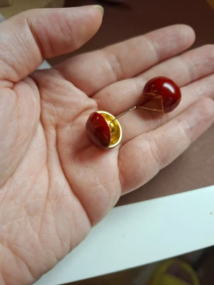 Runda röda örhängen med gulddetalj - Unika örhängen i rund form med djup röd färg och insida i guldton. De har en modern, halvmåne-liknande design och är tillverkade i metall och plast. Perfekta för dig som gillar statement-smycken och vill sticka ut med något annorlunda.