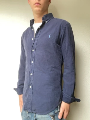Blå skjorta från Ralph Lauren - Blå skjorta från Ralph lauren som passar perfekt till sommar kvällarna. Modellen på bilderna är 178cm och väger cirka 70kg. Hör gärna av er vid intresse eller frågor!