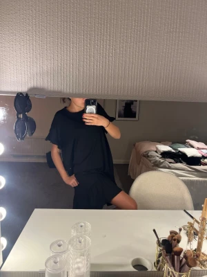 Svart kort klänning i bomull - En svart, kort klänning med loose passform och rund hals. Klänningen har korta ärmar och är tillverkad i mjuk bomull, perfekt för en avslappnad och stilren look.