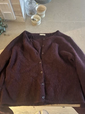 Mörklila kofta från Gina Tricot - Mysig mörklila kofta från Gina Tricot med knappar framtill. Koftan är tillverkad i ett fluffigt, stickat material och har en avslappnad passform. Perfekt att slänga på sig när det är kyligt ute.