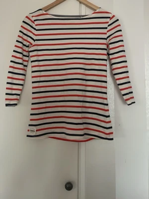 Randig långärmad topp från Petit Bateau - Säljer en långärmad topp från Petit Bateau med klassiskt randigt mönster i vitt, rött och marinblått. Toppen har rund halsringning och är tillverkad i mjuk bomull. Perfekt för en avslappnad och stilren look.