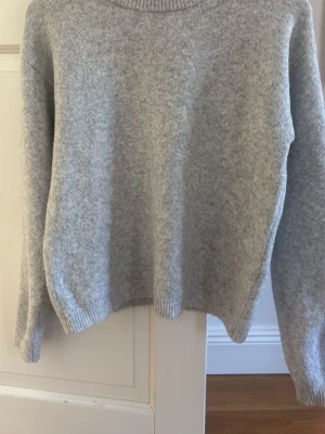 Ljusgrå stickad tröja Kappahl - Mysig ljusgrå stickad tröja från Kappahl med rund halsringning och ribbade muddar. Perfekt för lager-på-lager och enkel att matcha med jeans eller kjol. Klassisk och stilren modell som passar till många tillfällen.