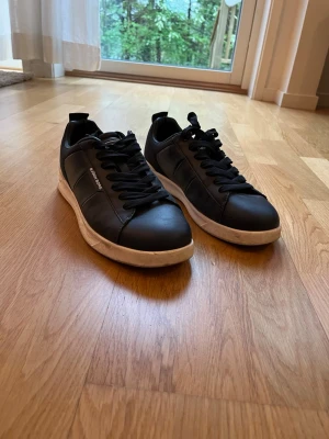 Mörkblå björn Borg skor  - Snygga svarta sneakers från Björn Borg med vita sulor och svarta skosnören. Skorna har en stilren design med diskret logga på sidan och ovandel i läderliknande material samt meshdetaljer vid hälen. Perfekta för en clean och modern look. Pris kan diskuteras 