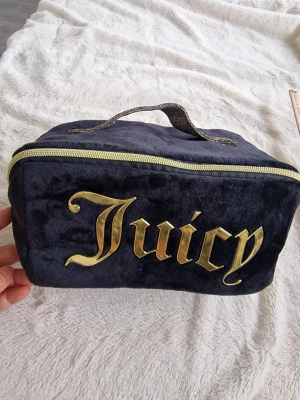 Juicy Couture svart sammet necessär - Snygg svart necessär i mjuk sammet från Juicy Couture med stort guldfärgat Juicy-tryck på framsidan. Väskan har dragkedja i guld och ett glittrigt handtag upptill. Perfekt för smink eller småprylar.
