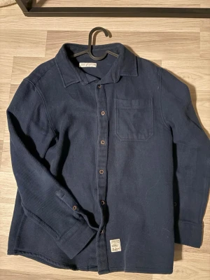 Mörkblå overshirt från Zara - Stilren mörkblå overshirt från Zara i mjuk manchester. Skjortan har klassisk krage, bröstficka och knappar framtill. Säljer nu just för att jag har växt ur den. Hör av er vid minsta fundering ✨