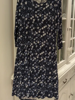 Mörkblå prickig klänning Isolde - Mörkblå klänning från Isolde med vitt och blått prickigt mönster. Klänningen har trekvartsärm och en ledig passform som ger en avslappnad look. Perfekt för dig som gillar mönstrade plagg med lite extra karaktär.