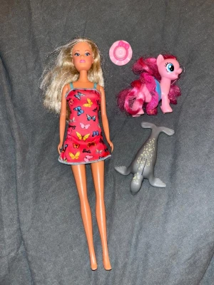 Barbiedocka mm - Säljer en Barbiedocka-man kan trycka på magen, varför vet jag inte riktigt. Medföljer en rosa My Little Pony-figur, en grå plastval och en liten rosa accessoar till håret-antingen dockan hår eller ens egna. Perfekt för dig som gillar att leka med dockor och figurer. Skickar även med en extra klänning till barbien- se sista bild.