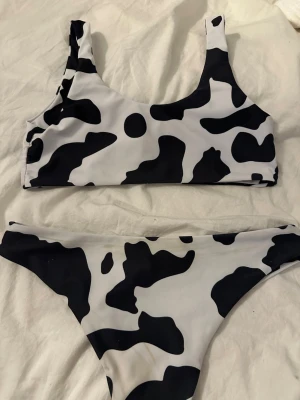 Svartvit bikini med ko-mönster - Säljer en trendig bikini med svartvita ko-fläckar. Överdelen har breda axelband och rundad halsringning, medan underdelen har en klassisk bikini-trosa modell. Perfekt för dig som vill sticka ut på stranden!