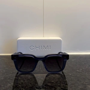Mörkblå solglasögon från Chimi och transparenta solglasögon från chimi - Snygga  solglasögon från Chimi med rektangulär form och tjock båge. Glasögonen har en stilren och modern design som passar perfekt till alla tillfällen. Kommer med ett vitt Chimi-fodral. Modell 04