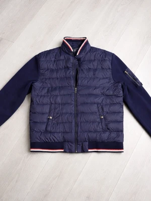 Mörkblå pufferjacka från Polo Ralph Lauren - Snygg mörkblå pufferjacka från Polo Ralph Lauren med quiltad kropp och släta ärmar. Jackan har ståkrage med rödvit rand, dragkedja framtill, två fickor med tryckknapp och broderad logga på bröstet. Perfekt för kalla dagar.