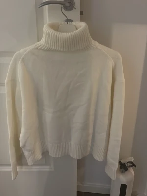 ALDRIG ANVÄND - Vit polotröja i stickat material - Säljer en krämvit stickad polotröja med hög, ribbad krage och breda muddar vid ärmslut och nederkant. Tröjan har en avslappnad passform och är perfekt för kalla dagar. Enkel och stilren design som passar till det mesta. Aldrig använd då den var för kort i armar på mig 💕💕💕