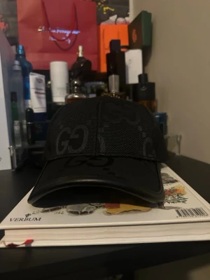  Gucci med GG Jumbo - Säljer en svart keps från Gucci med det klassiska GG-mönstret över hela kepsen. Kepsen har böjd skärm och mesh-paneler på sidorna för extra ventilation. Tillverkad i bomull och polyester med elastan för stretch. Perfekt för dig som gillar exklusiva accessoarer.