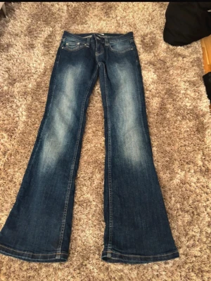 Blå bootcut jeans med lågmidja - Säljer ett par blå bootcut jeans med lågmidja. Jeansen har klassiska fem fickor och kontrastsömmar på bakfickorna. Skriv för fler frågor och bilder.💕