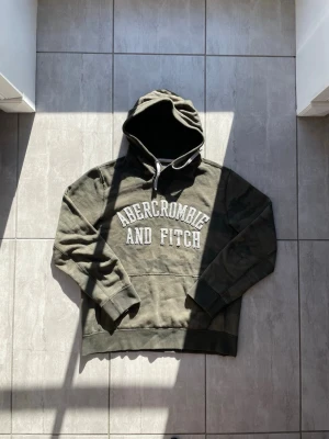 Camouflage hoodie från Abercrombie & Fitch - Camouflage hoodie från Abercrombie & Fitch med stor vit logga på bröstet. Klassisk känguruficka framtill, vit dragsko i huvan och mjukt material. Perfekt för en chill och avslappnad stil. Vid frågor eller fu deribgwr skriv gärna