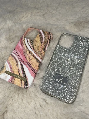2 snygga mobilskal Ideal & Swarovski - Säljer två jättefina mobilskal : ett från Ideal of Sweden med marmormönster i rosa, vitt och guld, samt ett från Swarovski täckt av glittrande silverfärgade stenar. Obs! Swarovski mobilskal är synligt använt kolla bild 5. Lägg gärna bud 🩷