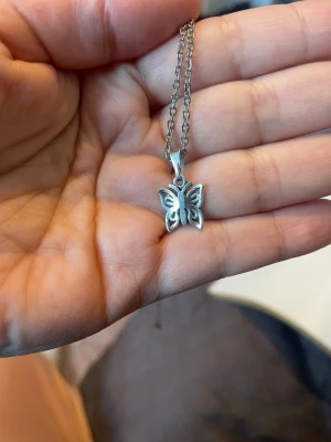 Silverfärgat fjärilshalsband - Snyggt halsband med en silverfärgad fjäril som hänge. Kedjan är tunn och har en klassisk länkdesign. Fjärilen har ett detaljerat, utskuret mönster som ger ett stilrent och trendigt intryck. Perfekt accessoar för dig som gillar naturinspirerade smycken.