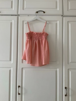 Ljusrosa linnetopp med smock✨✨ - Söt ljusrosa linnetopp med smala axelband och smockad överdel. Toppen har en luftig passform och är tillverkad i ett strukturerat tyg som ger en trendig känsla. Perfekt för varma dagar och enkel att styla med jeans eller kjol.